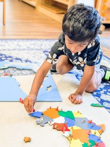 Primary student on the floor engaged with a map puzzle of Africa.