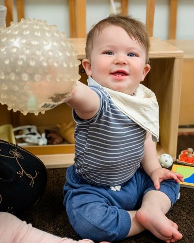 Infant sitting on the floor holding a rubber ball with pride.
