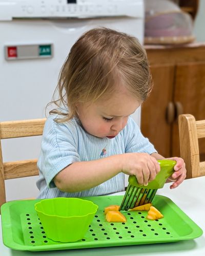 Toddler using practical ife skills to cut a melon on her own.
